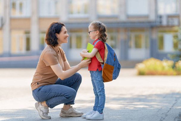 Parent and pupil of primary school go hand in hand. Woman and girl with backpack behind the back. Beginning of lessons. First day of fall. - 写真・画像