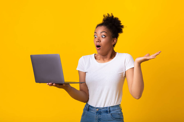 Έκπληκτη μαύρη κοπέλα αισθάνεται σοκαρισμένη κρατώντας φορητό υπολογιστή - Φωτογραφία, εικόνα