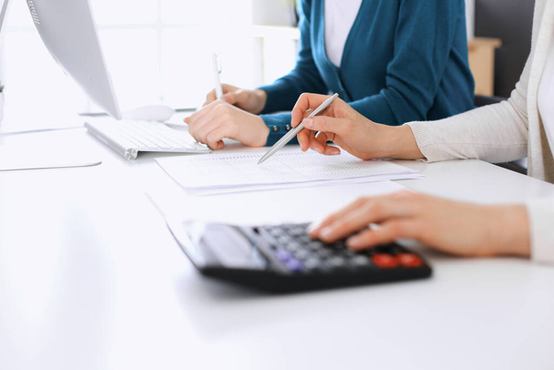 Accountant checking financial statement or counting by calculator income for tax form, hands closeup. Business woman sitting and working with colleague at the desk in office. Tax and Audit concept - Foto, afbeelding