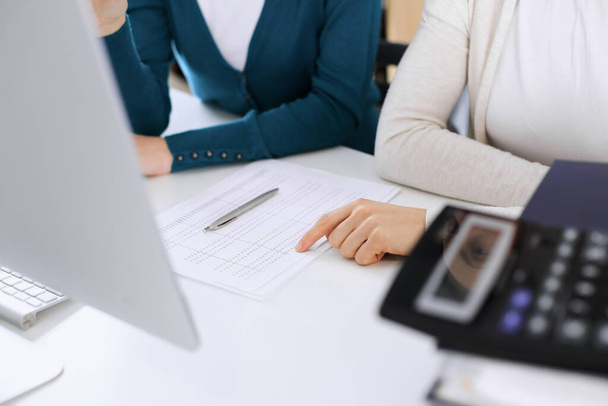 Accountant checking financial statement or counting by calculator income for tax form, hands closeup. Business woman sitting and working with colleague at the desk in office. Tax and Audit concept - Φωτογραφία, εικόνα