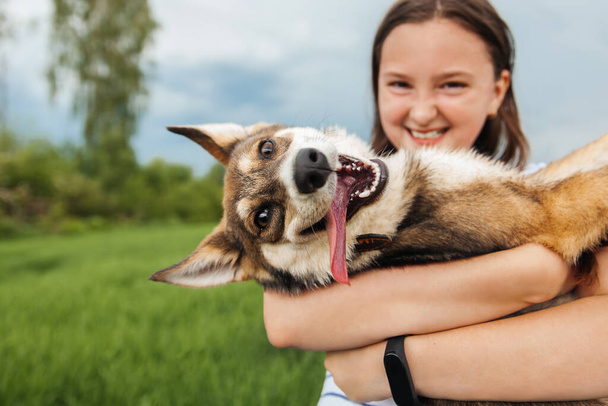 Smiling teenage girl holding a happy dog in her arms, looking at the camera - Valokuva, kuva