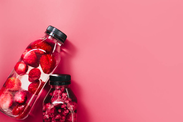 Detox infuso di acqua dolce con fragole lamponi in bicchieri scintillanti e bottiglie su sfondo rosa colorato, spazio copia. Bevanda estiva fredda. Acqua minerale. Vista dall'alto. - Foto, immagini