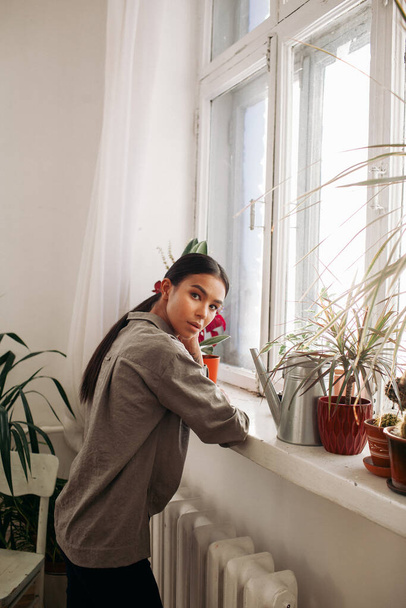 стильная молодая женщина у большого окна с растениями - Фото, изображение