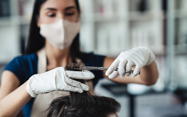 Hairdresser in medical mask cutting hair of male customer, close up - Фото, зображення