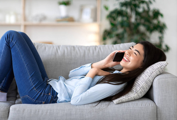 Positivo asiatico ragazza relax su divano, parlando sul cellulare con gli amici - Foto, immagini