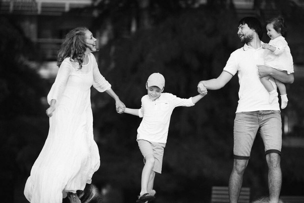 Famiglia felice in vestiti bianchi che si tiene per mano correndo avanti e ridendo - Foto, immagini