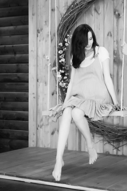 donna incinta seduta su un'altalena su uno sfondo di legno - Foto, immagini
