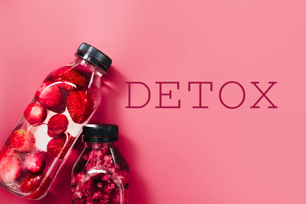 Detox infused fresh water with strawberries raspberries in sparkling glasses and bottles on colorful pink background, copy space. Cold summer drink. Mineral water. Top view. - Fotó, kép