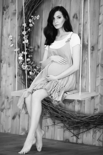 femme enceinte assise sur une balançoire sur un fond en bois - Photo, image