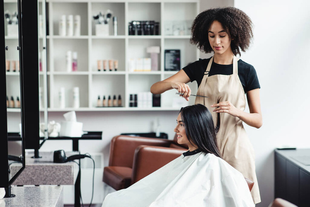 Mujer joven disfrutando de corte de pelo en el salón de belleza con maestro negro - Foto, Imagen