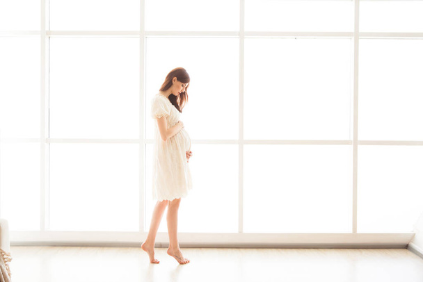 bela mulher grávida em um vestido brilhante está de pé no fundo de uma janela panorâmica - Foto, Imagem