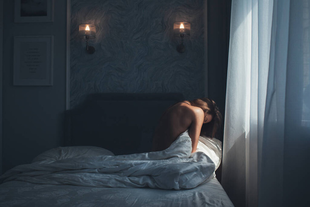bela mulher loira encontra-se cama de manhã envolto quarto cobertor de seda branca com quarto moderno interior com os olhos fechados em frente à janela que o sol é brilho - Foto, Imagem