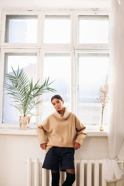 hermosa mujer en suéter permanecer cerca de la ventana en el día  - Foto, imagen