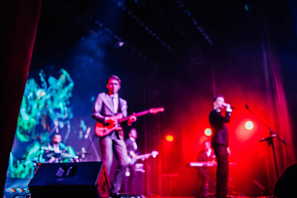 θολή φωτεινή πολύχρωμη φωτογραφία του τραγουδιστή και ροκ συγκρότημα που εκτελεί επί σκηνής στο κόκκινο μπλε μωβ φώτα των φωτεινών προβολέων - Φωτογραφία, εικόνα