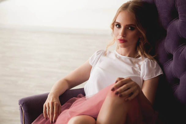 beautiful attractive young blonde girl sitting on violet chair - 写真・画像