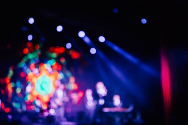 foto colorida brilhante borrada do cantor e da banda de rock que executam no palco nas luzes roxas azuis vermelhas dos holofotes brilhantes - Foto, Imagem