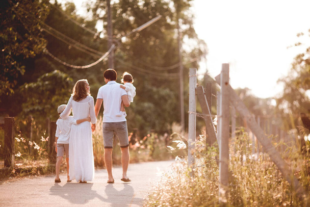 Happy family in white clothes walking together on the road at sunset - Foto, Imagen