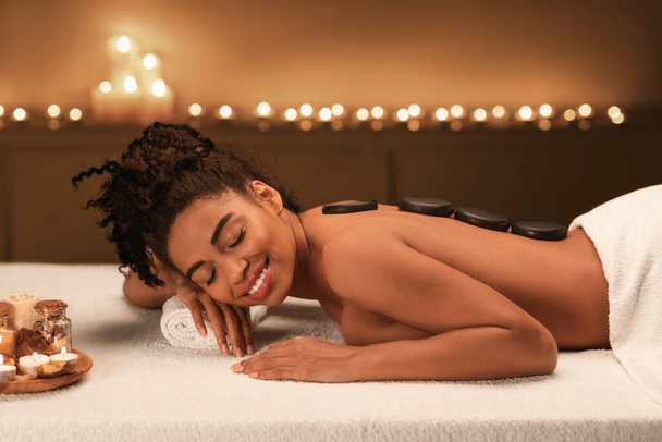 czarny młody kobieta otrzymywać gorący kamień masaż w spa - Zdjęcie, obraz