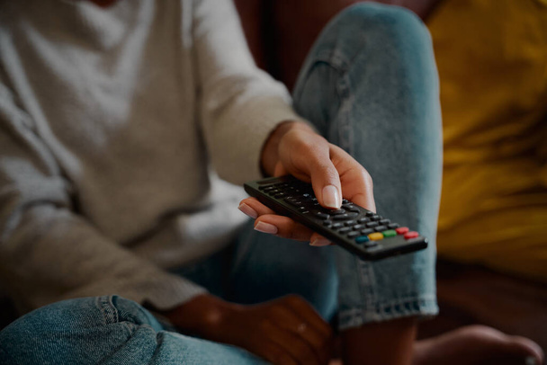 Closeup of young female hand holding remote control and changing channel at home watching television alone - 写真・画像