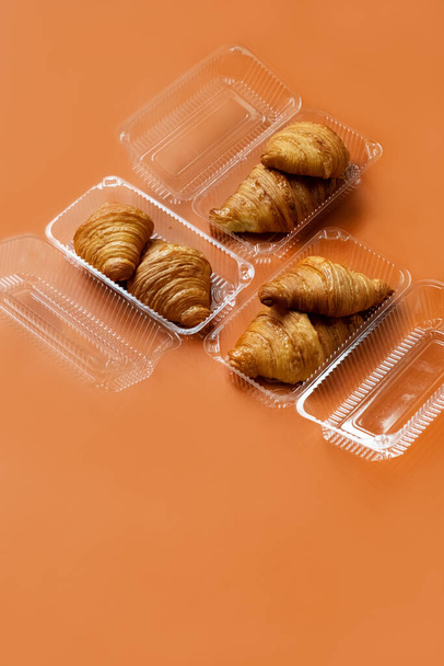 Croissants fraîchement cuits dans un emballage en plastique sur fond orange. Concept de nourriture à emporter. Croissants français et américains sont appréciés dans le monde entier.Croissants arrière-plan : vue sur le dessus, plan plat - Photo, image
