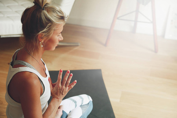 Blonde woman is sitting and holding her palms together. Girl with hair ponytail doing yoga at home. Space for text. - Foto, Imagem