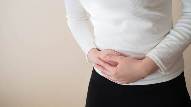 若い女性の苦しみは灰色の背景に腹部の痛みを形成しますw/コピースペース.腹部の痛みの原因は、月経困難症を含みます,子宮内膜症, PMSまたは卵巣嚢胞.婦人科・ヘルスケアの概念. - 写真・画像