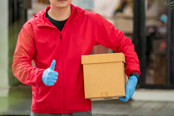 Close up delivery man Het dragen van blauwe handschoenen in rode doek met een doos pakket - Foto, afbeelding