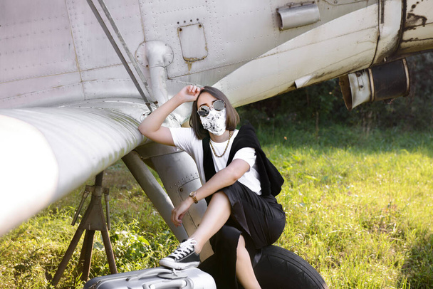 Giovane donna in abiti moderni, occhiali e una maschera seduta su un aereo d'epoca e in attesa - Foto, immagini