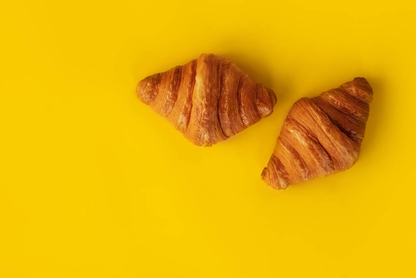Frissen sült croissant sárga alapon. Az ételminimalizmus fogalmai. Francia és amerikai croissant élvezik világszerte. Croissants háttér: felülnézet, lapos laikus - Fotó, kép