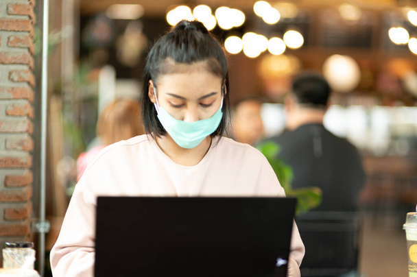 Nainen yllään kirurginen naamio kahvilassa ostoksia verkossa kannettavan - Valokuva, kuva