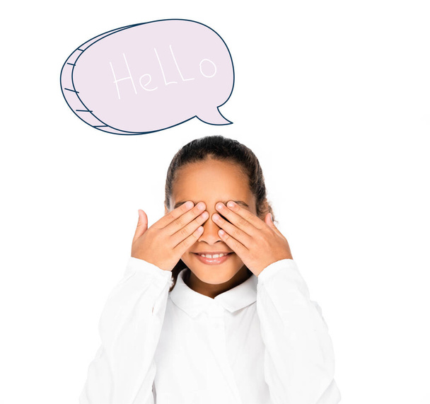 african schoolgirl smiling while covering eyes with hands isolated on white, speech bubble with hello lettering illustration - Фото, изображение