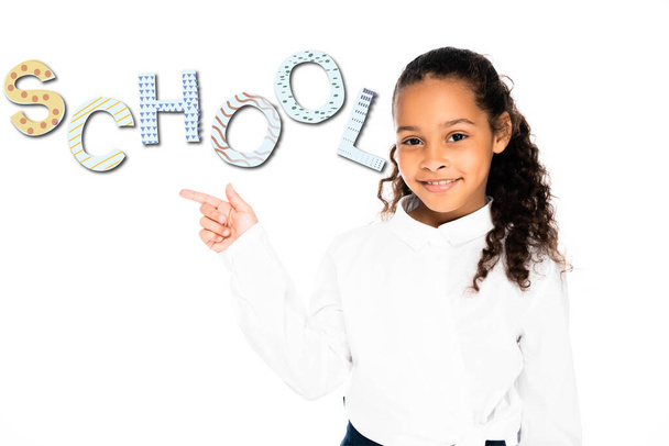 african american schoolgirl pointing with finger at school lettering while looking at camera isolated on white - Fotoğraf, Görsel