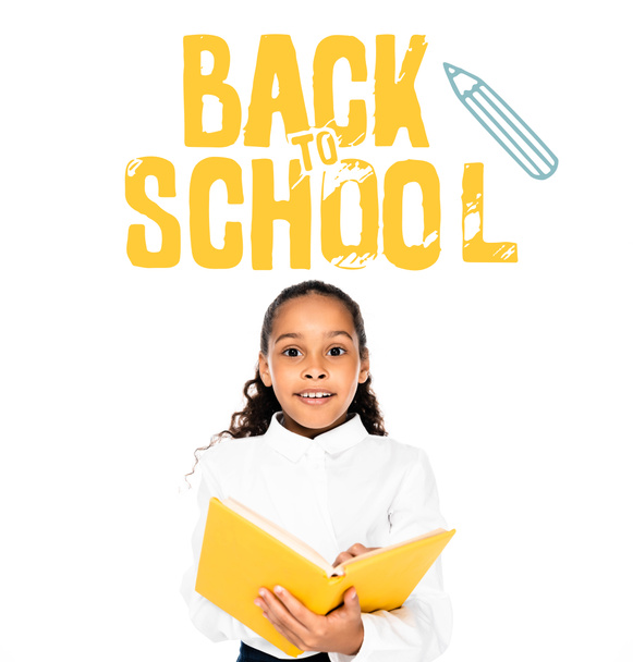 excited african american schoolgirl holding book and looking at camera isolated on white, back to school illustration - Foto, immagini
