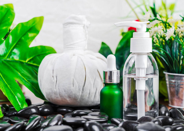 Thaï Spa massage réglage avec compte-gouttes bouteille d'huile sérique maquette ou huile essentielle et thaï boules de compression à base de plantes sur pierre noire sur fond de feuilles vertes - Photo, image