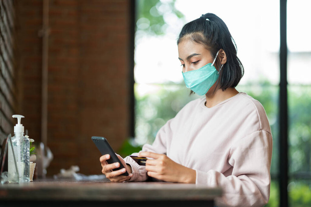 Donna che indossa maschera chirurgica in caffè shopping online con il telefono cellulare - Foto, immagini