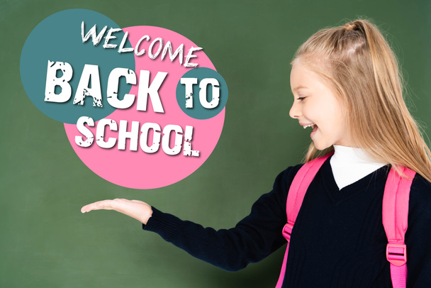 schoolgirl pointing with hand at welcome back to school illustration on green chalkboard  - Photo, Image