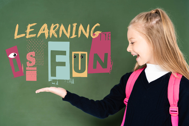 schoolgirl pointing with hand at learning is fun illustration on green chalkboard  - Φωτογραφία, εικόνα