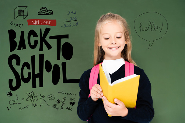 schoolgirl reading book near green chalkboard with back to school illustration - Photo, Image