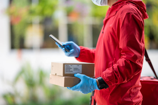 Close up delivery man Wearing blue gloves in red cloth Searching for customer address by mobile phone - Foto, afbeelding