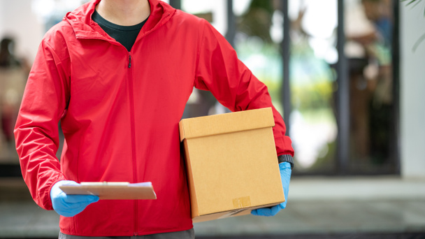 чоловік доставки в сині рукавички в червоній тканині тримає картонні коробки
 - Фото, зображення