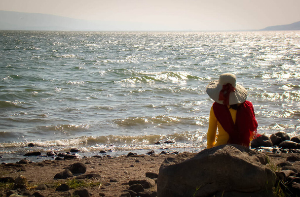 Erstaunliche Frau mit Hut, die das Meer von Galilea in Israel betrachtet. Einsamkeit und Gebet - Foto, Bild