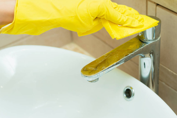 Joku pesee lavuaaria keltaisissa hanskoissa. Joku siivoaa kylpyhuonetta pesuaineilla.. - Valokuva, kuva