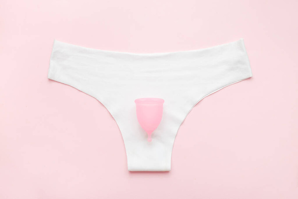 Pantalón blanco con copa menstrual sobre fondo de color rosa pastel. Colocación plana, pantalón, copa menstrual. Menstruación, higiene femenina, salud de la mujer, concepto de cero residuos - Foto, Imagen