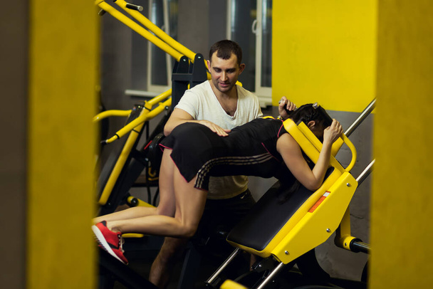 Deporte, fitness, trabajo en equipo, concepto de levantamiento de pesas: mujer joven y entrenador personal con músculos flexionantes en el gimnasio - Foto, imagen