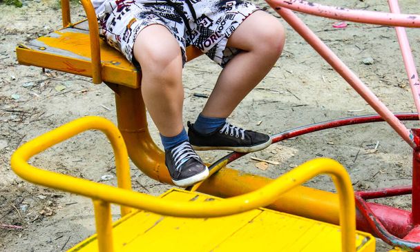 Gyerekek, akik egy alacsony körhintán pörögnek a játszótéren. Az ülő gyermekek lábainak részei. Szelektív lövés. - Fotó, kép