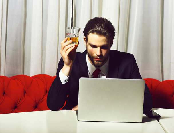 bearded man, businessman holding glass of whiskey works at laptop - Foto, Imagen