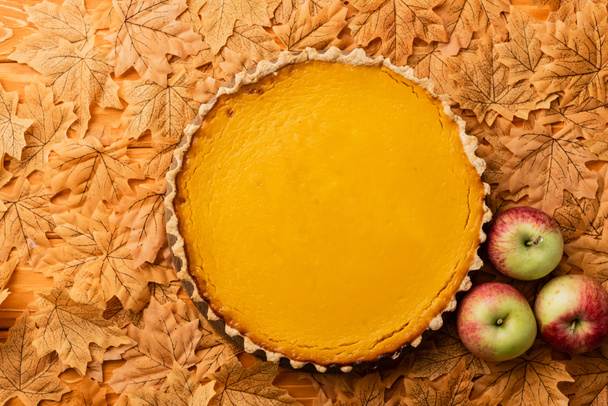 top view of thanksgiving pumpkin pie with apples and autumnal foliage on wooden background - Фото, зображення