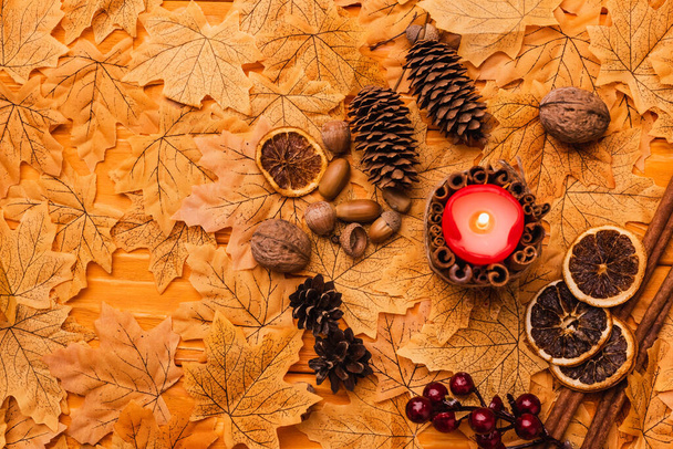 top view of burning candle with autumnal brown decoration on golden foliage - Foto, Imagen