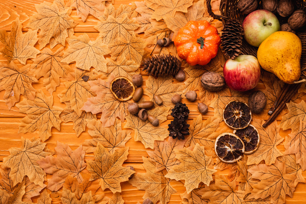 top view of autumnal decoration and food scattered from wicker basket on golden foliage on wooden background - 写真・画像