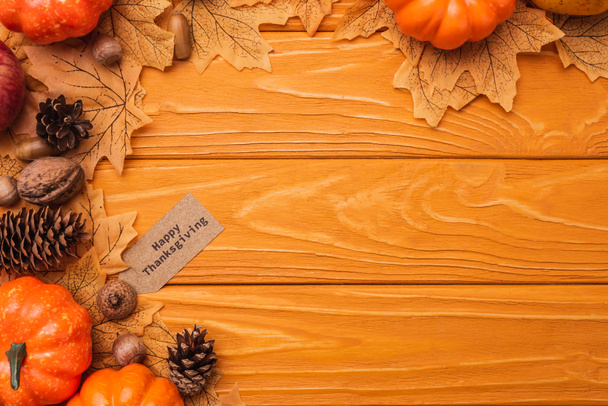 bovenaanzicht van pompoenen, herfstdecoratie en gelukkige Thanksgiving kaart op houten achtergrond - Foto, afbeelding